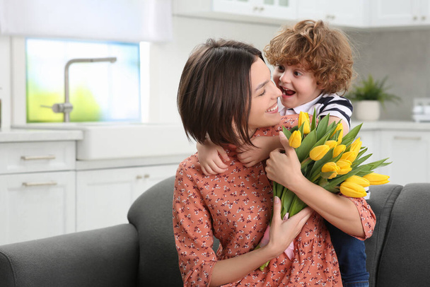 Little son congratulating his mom with Mother`s day at home. Woman holding bouquet of yellow tulips - Photo, Image