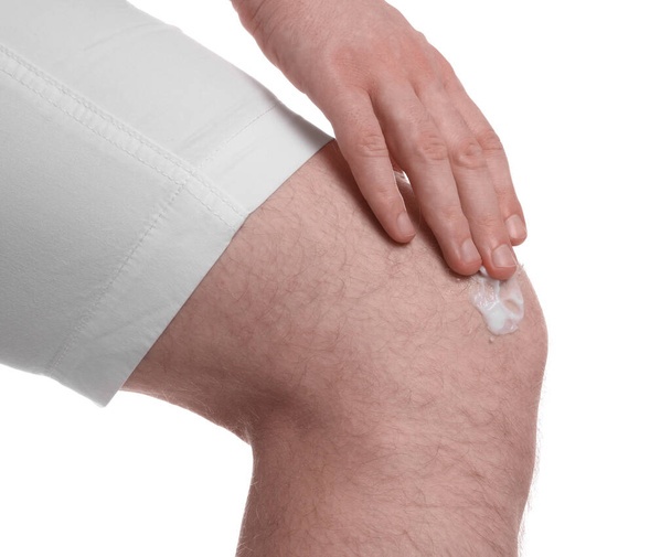 Man applying ointment onto his knee on white background, closeup - Фото, изображение