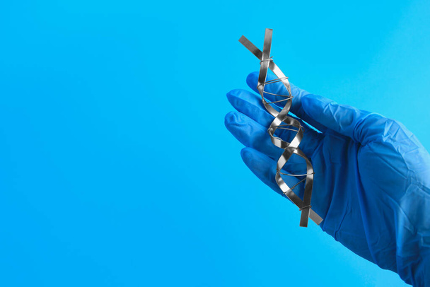 Scientist with DNA molecular chain model made of metal on blue background, closeup. Space for text - Foto, imagen