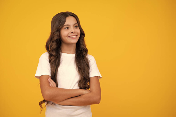 Confident child keep arms crossed, isolated on yellow background, empty space. Little caucasian teenage girl 12, 13, 14 years old hold hands crossed. Children studio portrait. Childhood lifestyle - Photo, image