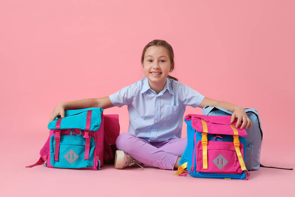 Little girl with backpacks sitting on pink background - Фото, изображение