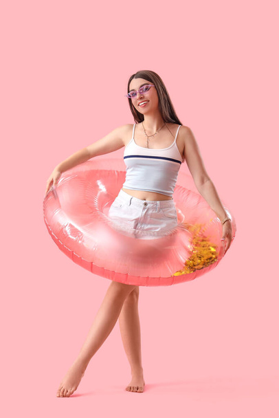 Mujer joven con anillo inflable sobre fondo rosa - Foto, Imagen