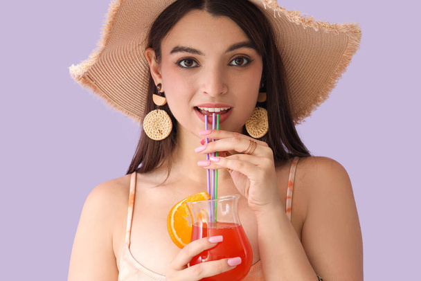 Young woman drinking summer cocktail on lilac background, closeup - 写真・画像