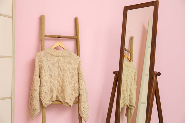 Sweater hanging on wooden ladder and mirror near pink wall in room - Foto, afbeelding