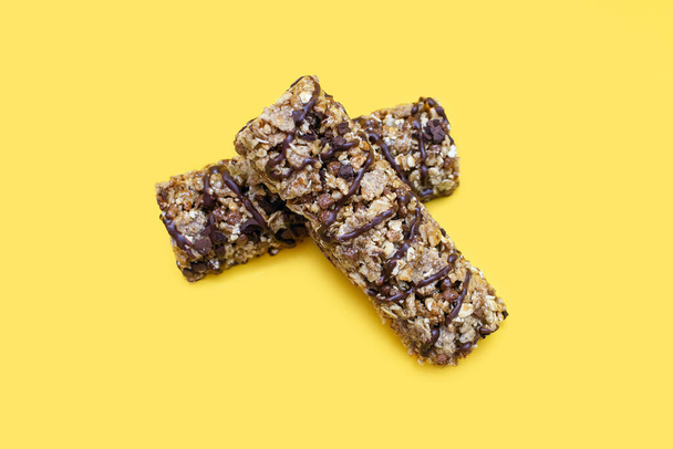 Two bars of whole oatmeal and chocolate on a yellow isolated background. Delicious healthy snack or energy replenishment. Whole grain energy bars with chocolate - Photo, Image