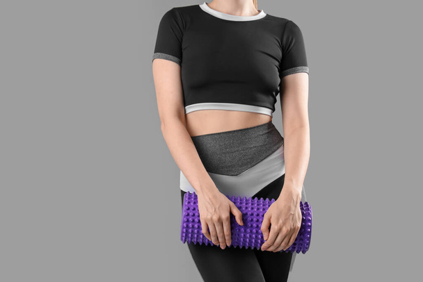 Young woman in sportswear and with foam roller on grey background - Photo, Image