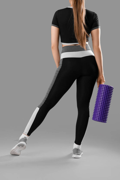 Młoda kobieta w odzieży sportowej i z wałkiem piankowym na szarym tle, widok z tyłu - Zdjęcie, obraz