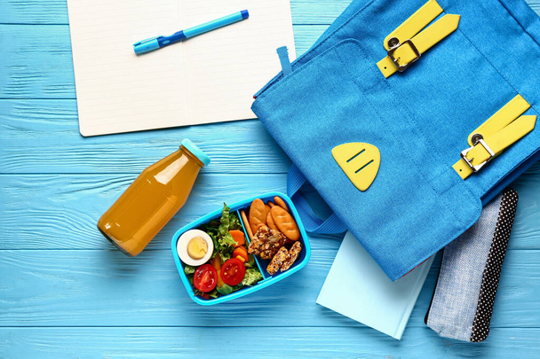 Backpack, stationery and lunchbox with tasty food on blue wooden background - Zdjęcie, obraz