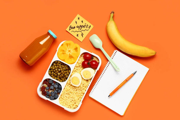 Stationery, tasty food in lunchbox and sticky note with text BON APPETIT on orange background - Photo, Image