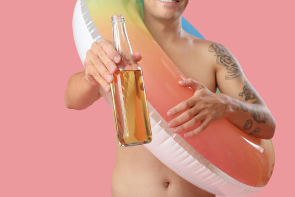 Giovane con birra e anello di nuoto su sfondo rosa, primo piano - Foto, immagini
