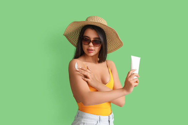 Hermosa mujer joven aplicando crema protector solar sobre fondo verde - Foto, Imagen