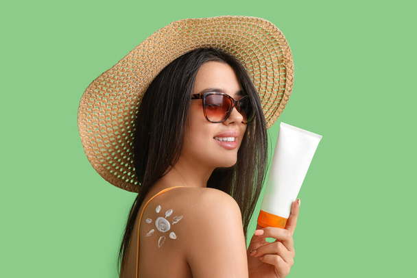 Beautiful young woman with sun made of sunscreen cream on green background - Foto, Imagem