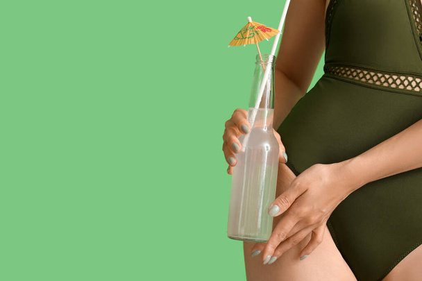 Hermosa mujer en traje de baño y con botella de limonada sobre fondo verde, primer plano - Foto, imagen