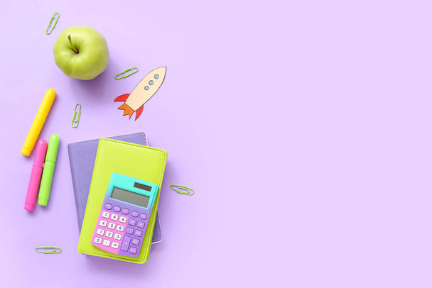 Paper rocket with school stationery and apple on purple background - Photo, Image