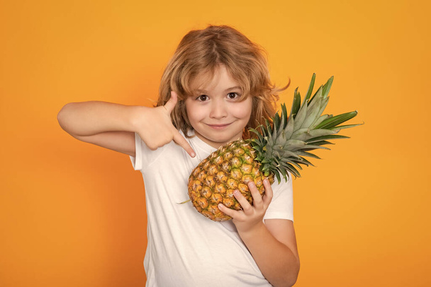 Kid with pineapple in studio. Studio portrait of cute child hold pineapple isolated on yellow background - Photo, Image