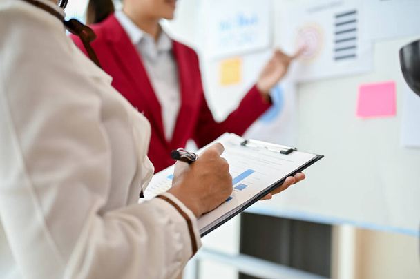 Close-up image of a professional businesswoman taking notes on documents while listening to her colleague present a project in the meeting. - Photo, Image