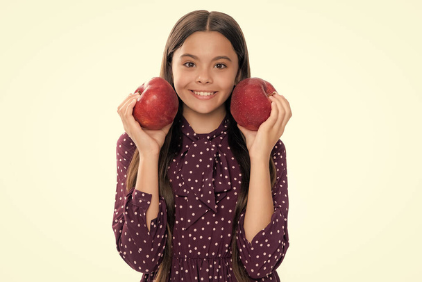 Дитяча дівчинка їсть яблуко над ізольованим білим студійним фоном. Теннеґер з фруктами. Портрет щасливої веселої усміхненої дівчинки-підлітка
 - Фото, зображення