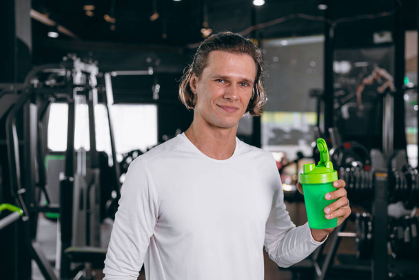 Gesunder Sportler mit Molke-Shaker-Flasche. glücklich trinkendes Molkenprotein für Muskelkräfteaufbau und fettarme Getränkemahlzeit im Fitnessstudio - Foto, Bild