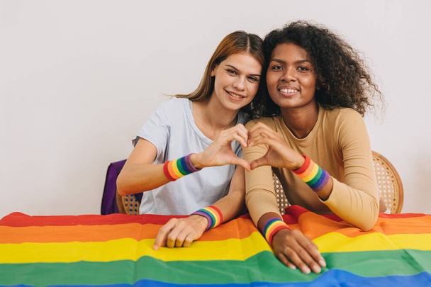 Портрет ЛГБТ-женщина рука сердце любви знак микс расы, живущей вместе с радужным флагом глядя камеры - Фото, изображение