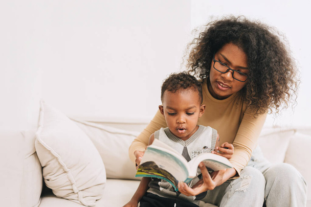 Wykształcenie matka daje nauka do małego chłopca ciekawe czytać książkę dla inteligentnego dziecka, afrykańskich czarnych ludzi rodziny - Zdjęcie, obraz