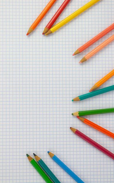 Notebook of squared sheets, to the right of the image has fallen colored pencils, photo representing the return to school, the pencils are forming a semi-circular space in the center of the image - Foto, afbeelding