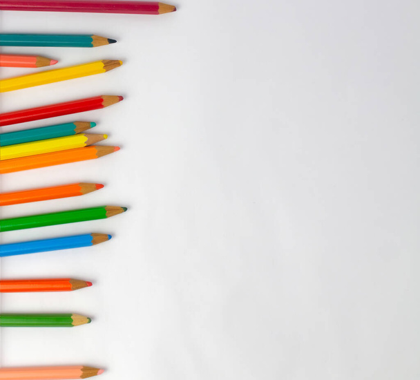 Children's colored pencils fallen on a white sheet to the left of the image forming a row, photo for back to school with space for texts, without background - Photo, image