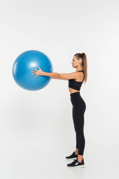 deportista en forma sosteniendo la pelota de fitness mientras hace ejercicio sobre fondo blanco, concepto de mujer atlética - Foto, Imagen