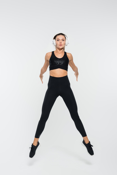 brunette woman in black active wear and headphones jumping on white background, sport  - Photo, Image