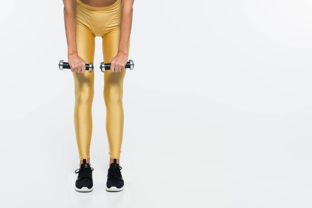 Vista recortada de la deportista en forma en entrenamiento de polainas amarillas con pesas sobre fondo blanco  - Foto, Imagen
