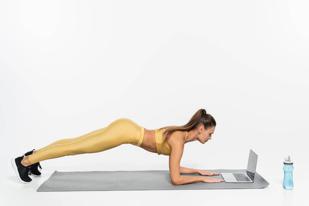 e-sport, nő csinál deszka fitnesz szőnyeg, fehér háttér, fizikai aktivitás koncepció, laptop  - Fotó, kép