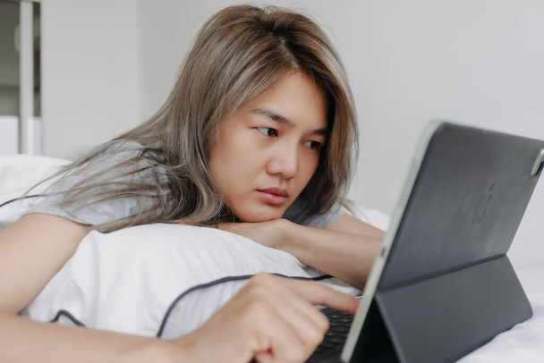 Asian woman working online on the tablet computer on the bed in the morning. - Φωτογραφία, εικόνα