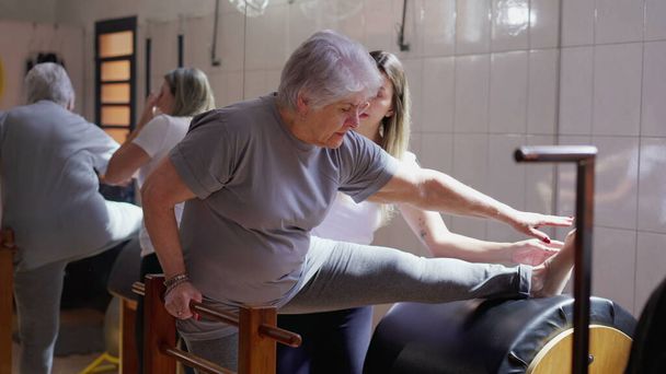 Mujer Pilates Coach guiando a una mujer mayor para estirar el cuerpo en la clase de fisioterapia. Entrenamiento de vejez rutina de salud y bienestar estilo de vida - Foto, Imagen