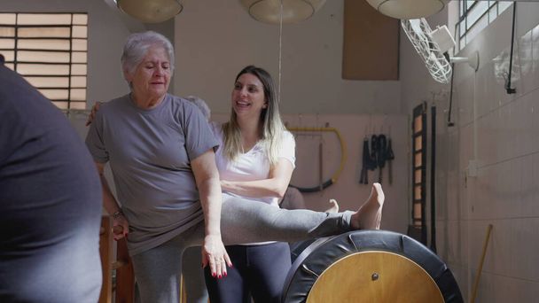 Инструктор по пилатесу, проводящий пожилую женщину в упражнениях на растяжку, способствующий активному образу жизни и гибкости в пожилом возрасте - Фото, изображение