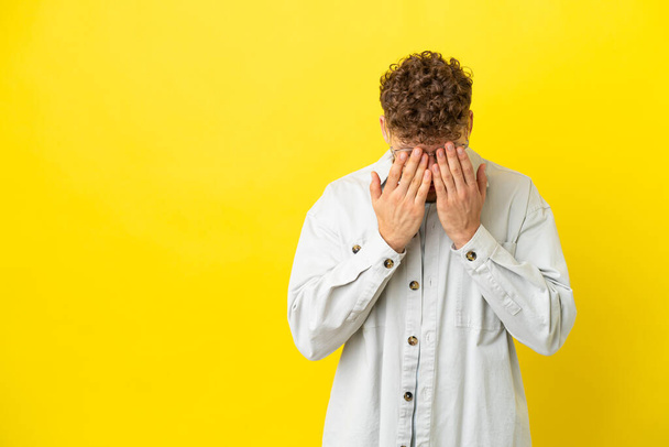 Young handsome caucasian man isolated on yellow background with tired and sick expression - Photo, Image