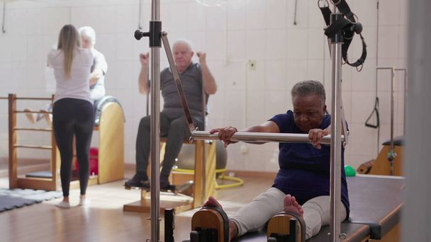 Старшие упражнения в группе пилатес, черная женщина, использующая машину для укрепления тела. Старый образ жизни тренировки - Фото, изображение