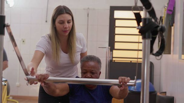 Entrenador de Pilates Femenino Asistiendo a Mujer Senior Negra en Entrenamiento de Máquina para Fortalecimiento Corporal y Flexibilidad - Foto, Imagen