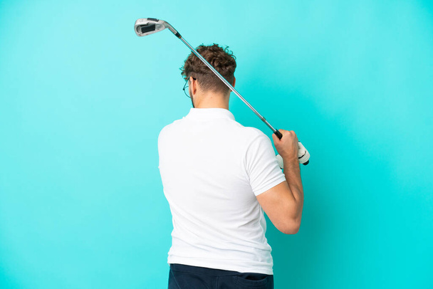 Jeune bel homme caucasien isolé sur fond bleu jouant au golf - Photo, image