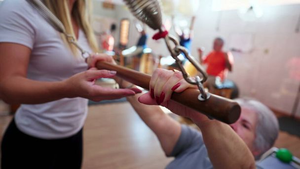 Zbliżenie starszej kobiety trzymającej sprzęt Pilates zorientowany przez trenera, aby rozciągnąć i wzmocnić ciało na starość rutynowych ćwiczeń - Zdjęcie, obraz