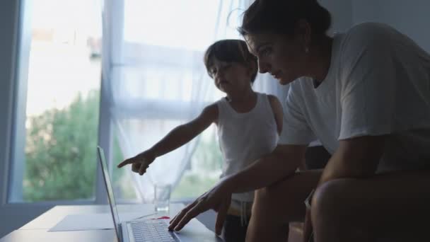 Мати мультизадачні завдання, що працюють з дому перед ноутбуком з дитиною - Кадри, відео