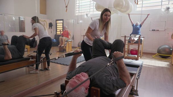 Yaşlılarla Grup Pilates Stüdyosu, Esneme ve Güçlendirme Makinesi ile Kıdemli Adam 'a Yardımcı Antrenör - Fotoğraf, Görsel