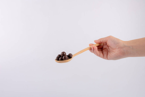 Boules de chocolat sur cuillère en bois à la main sur fond blanc. - Photo, image