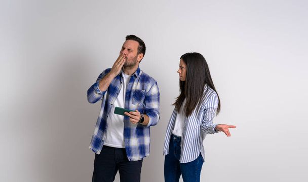 Сердита жінка жестикулює і дивиться на екстатичного геймера, який дме поцілунок, граючи в відеогру на мобільному телефоні. Серйозна дівчина дивиться щасливий хлопець грає на фоні - Фото, зображення