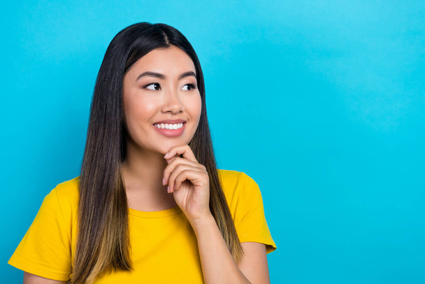 Photo de jeune asiatique beauté fille tenir bras doigt main sur menton look vide espace porter jaune t-shirt isolé bleu couleur fond. - Photo, image