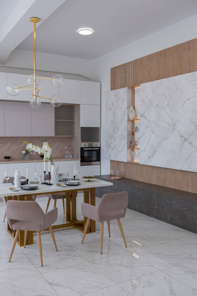 stylish kitchen and a set dining table in a light luxury interior design of a modern apartment in a minimalist style with marble trim and huge windows. daylight inside. - Fotó, kép
