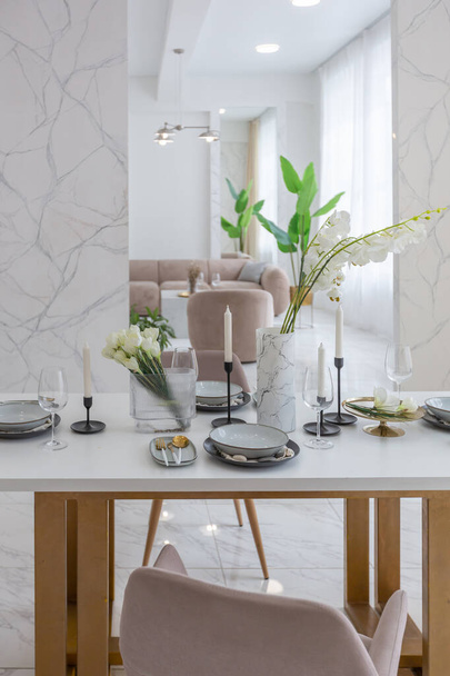 stylowa kuchnia i zestaw stół jadalny w jasnym luksusowym wystroju wnętrz nowoczesnego mieszkania w minimalistycznym stylu z marmurowym wykończeniem i ogromnymi oknami. światło dzienne wewnątrz. - Zdjęcie, obraz