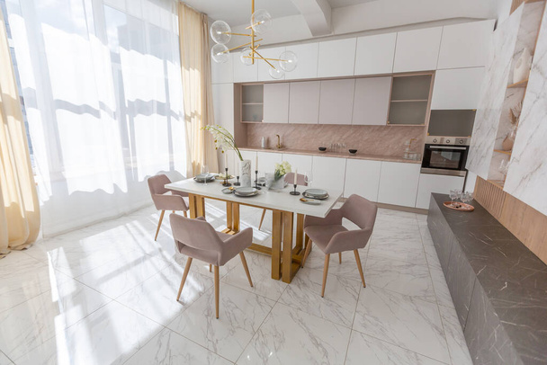 stylish kitchen and a set dining table in a light luxury interior design of a modern apartment in a minimalist style with marble trim and huge windows. daylight inside. - Fotoğraf, Görsel