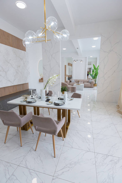stylish kitchen and a set dining table in a light luxury interior design of a modern apartment in a minimalist style with marble trim and huge windows. daylight inside. - Zdjęcie, obraz