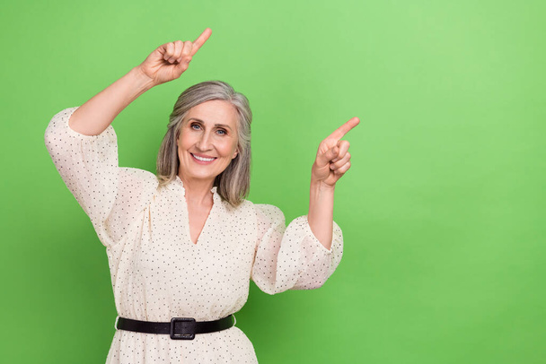 Photo portrait of lovely retired lady two fingers point empty space wear trendy white outfit isolated on green color background. - Foto, Imagem