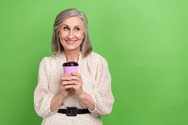 Portrait of pleasant good mood woman dressed stylish clothes hold cup of coffee look empty space isolated on green color background. - Photo, image