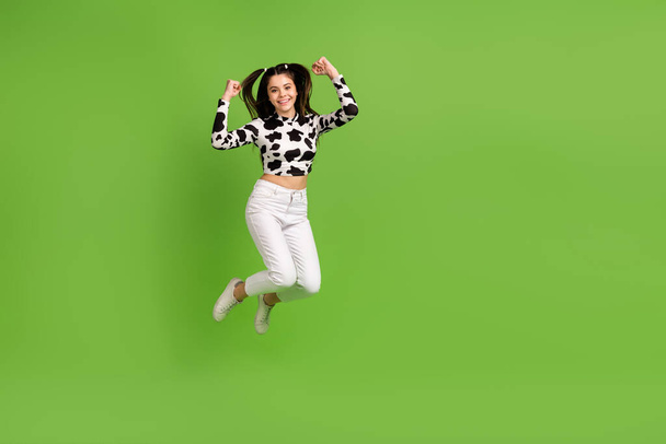 Foto de longitud completa de alegre chica de la suerte vestido de piel de vacuno superior saltando puños en alto espacio vacío aislado de color verde de fondo. - Foto, imagen